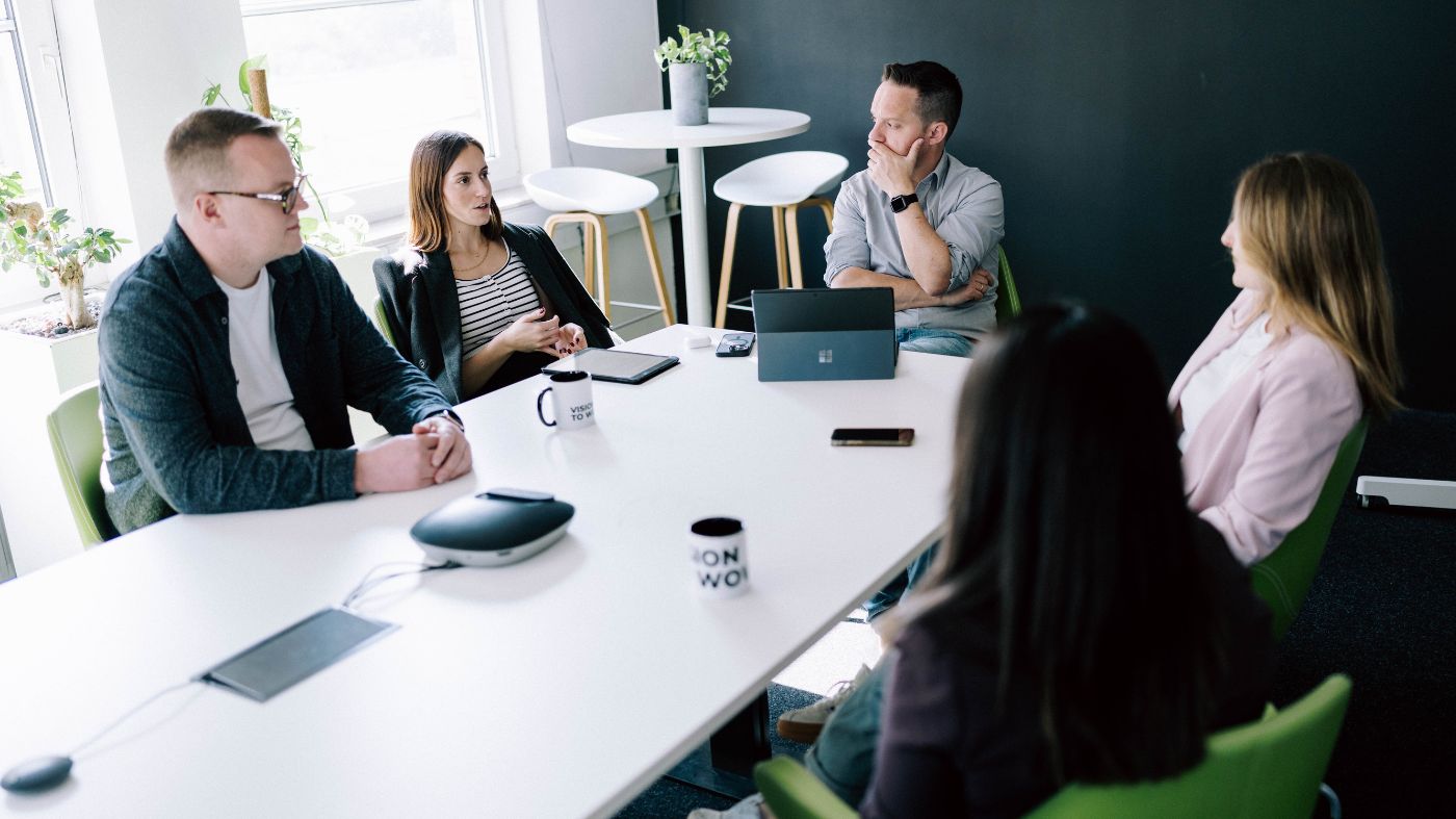 TYPO3-Experten im Meeting Fünf Personen sitzen in einem modernen Besprechungsraum an einem weißen Tisch und führen ein Teammeeting.
