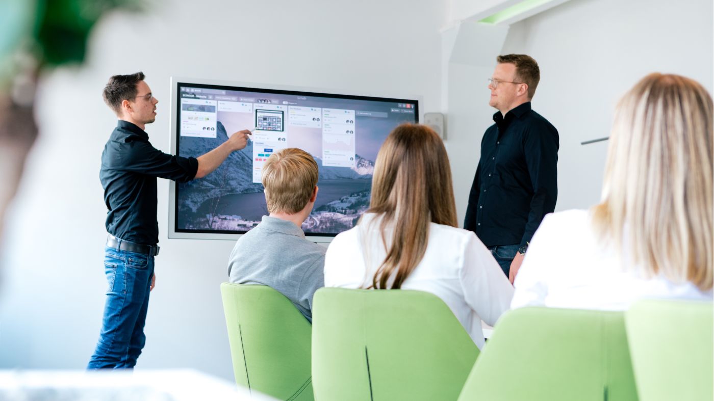 Experten in einem Teammeeting. Zwei Personen stehen vor einem Bildschirm und reden