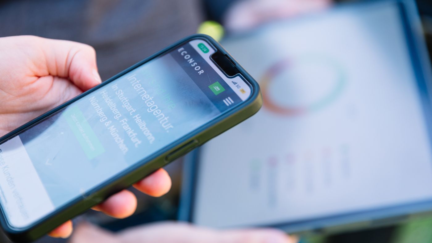 Smartphone mit geöffneter Website und Tablet im Hintergrund.